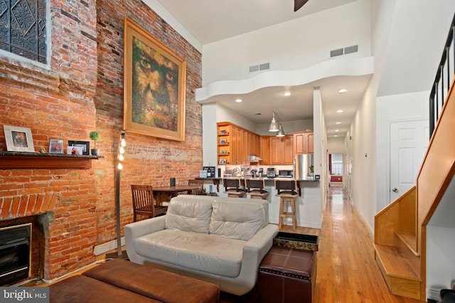 living room featuring light wood-type flooring, a fireplace, a towering ceiling, and brick wall