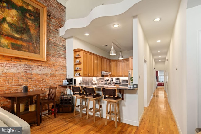 kitchen with light wood-type flooring, kitchen peninsula, a kitchen bar, appliances with stainless steel finishes, and brick wall