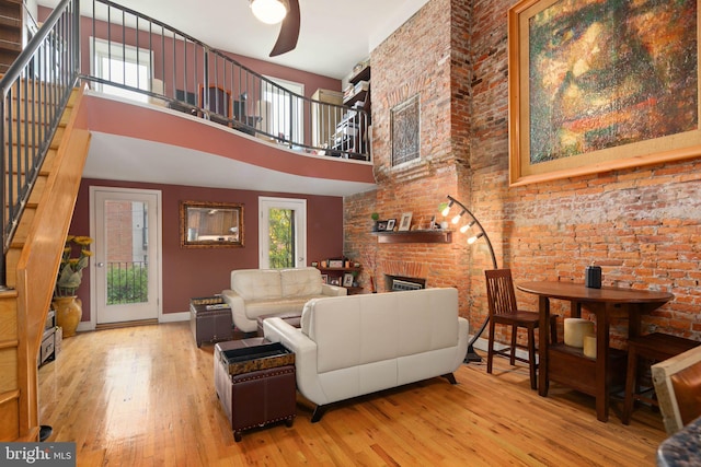 living room with a brick fireplace, a towering ceiling, hardwood / wood-style floors, ceiling fan, and brick wall