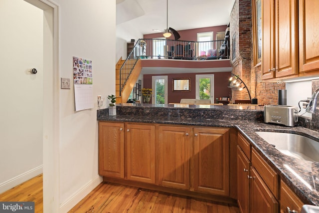 kitchen with light wood-type flooring, sink, kitchen peninsula, high vaulted ceiling, and dark stone countertops