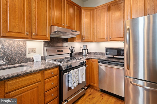 kitchen featuring sink, dark stone counters, appliances with stainless steel finishes, light wood-type flooring, and decorative backsplash