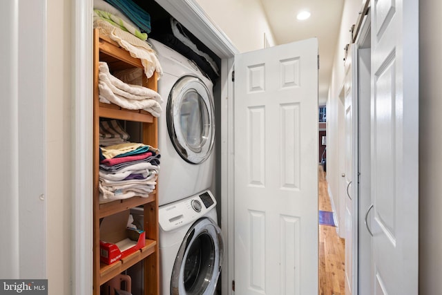 laundry area with hardwood / wood-style flooring, a barn door, and stacked washer / drying machine