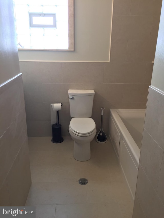 bathroom with tile walls, tile patterned floors, a bathtub, and toilet