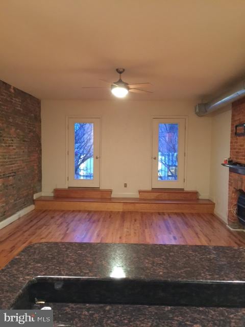 unfurnished living room with a fireplace, ceiling fan, light hardwood / wood-style flooring, and brick wall