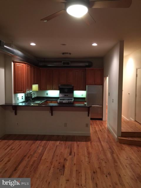 kitchen featuring light hardwood / wood-style flooring, a breakfast bar, kitchen peninsula, and appliances with stainless steel finishes