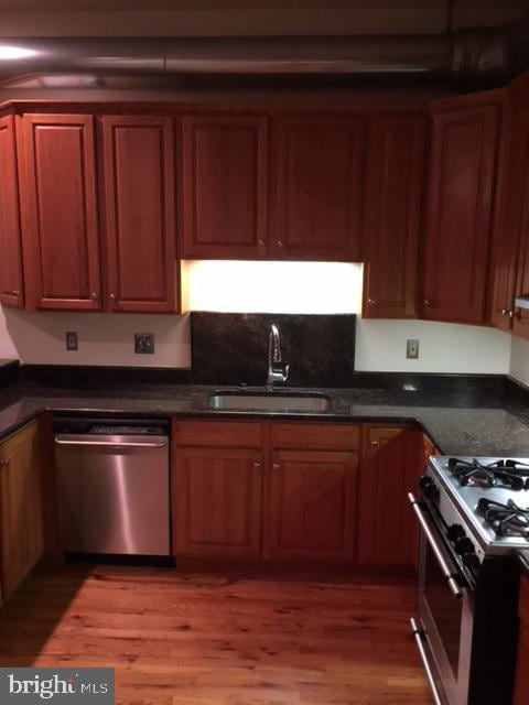 kitchen featuring wood-type flooring, appliances with stainless steel finishes, sink, and dark stone counters