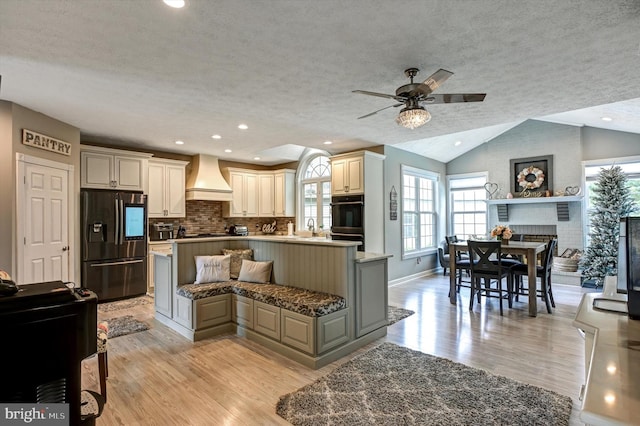 kitchen featuring lofted ceiling, stainless steel fridge, cream cabinets, custom range hood, and light hardwood / wood-style floors