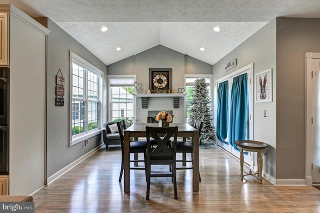 dining space with light hardwood / wood-style floors, a textured ceiling, lofted ceiling, and a fireplace