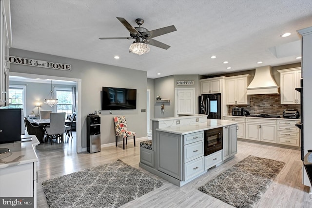 kitchen featuring black appliances, light hardwood / wood-style flooring, custom range hood, and a kitchen island