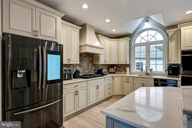 kitchen featuring light stone counters, black appliances, custom range hood, and sink