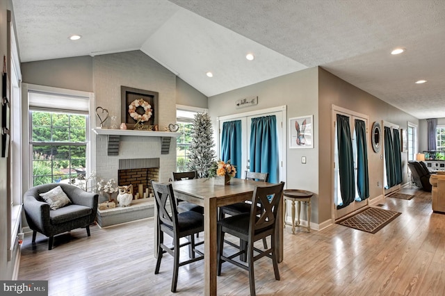 dining room featuring a healthy amount of sunlight, a textured ceiling, lofted ceiling, and light wood-type flooring