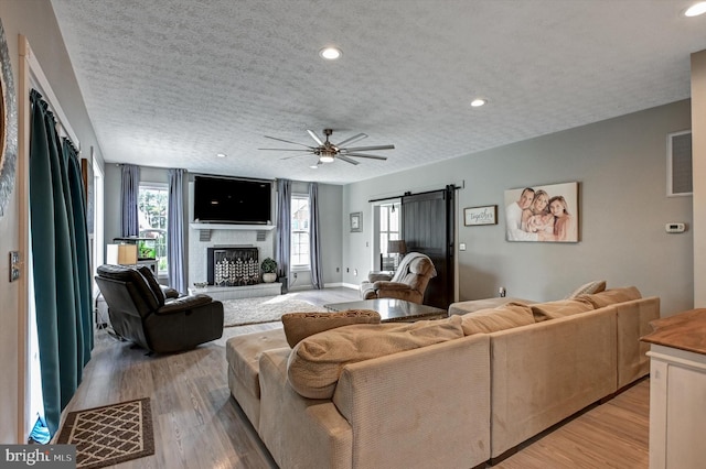 living room with a textured ceiling, a barn door, light wood-type flooring, and ceiling fan