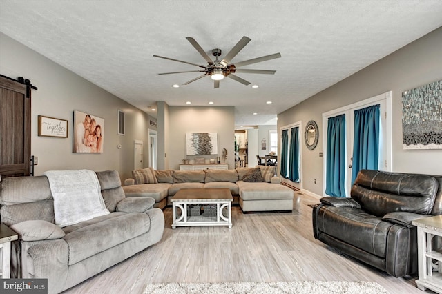 living room with light hardwood / wood-style floors, a textured ceiling, a barn door, and ceiling fan