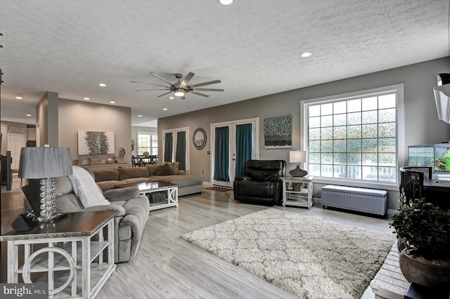 living room with a textured ceiling, ceiling fan, light wood-type flooring, and a wealth of natural light