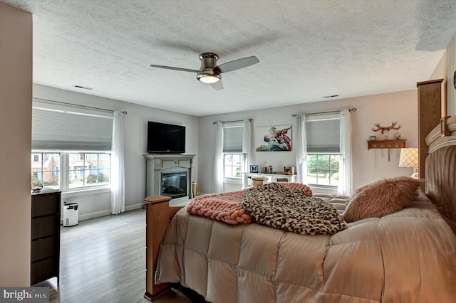 bedroom featuring light hardwood / wood-style flooring, a textured ceiling, multiple windows, and ceiling fan