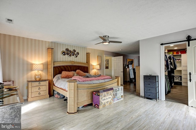 bedroom featuring a closet, a walk in closet, hardwood / wood-style floors, a barn door, and ceiling fan