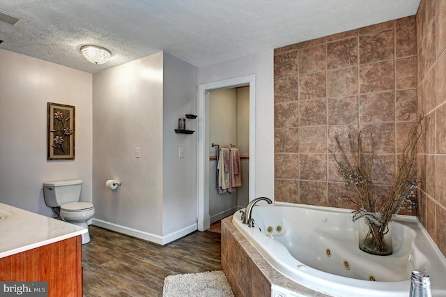 bathroom featuring wood-type flooring, a textured ceiling, toilet, tiled tub, and vanity