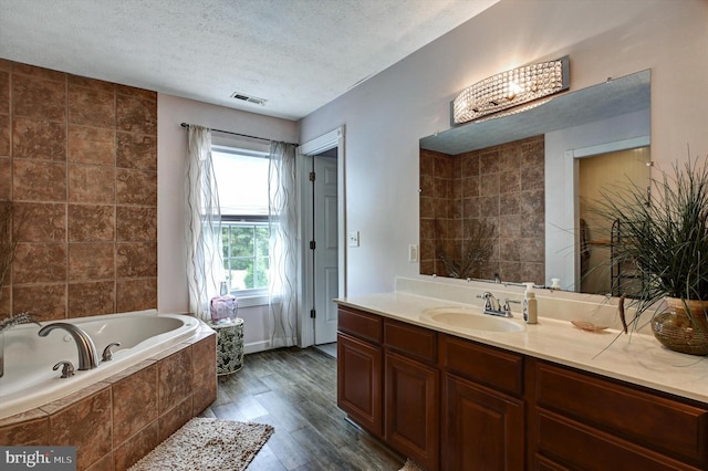 bathroom featuring vanity, hardwood / wood-style floors, a relaxing tiled tub, and a textured ceiling