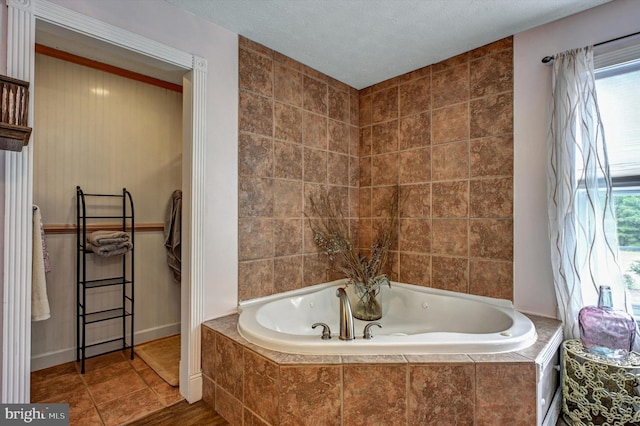 bathroom featuring a textured ceiling, a wealth of natural light, and tiled bath