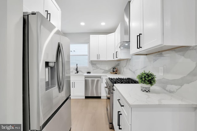 kitchen with light stone counters, white cabinetry, stainless steel appliances, light hardwood / wood-style floors, and decorative backsplash