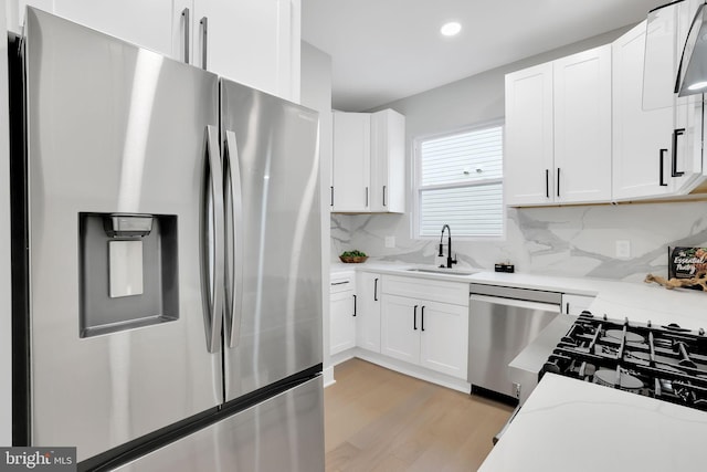 kitchen featuring white cabinets, sink, light hardwood / wood-style flooring, appliances with stainless steel finishes, and light stone countertops