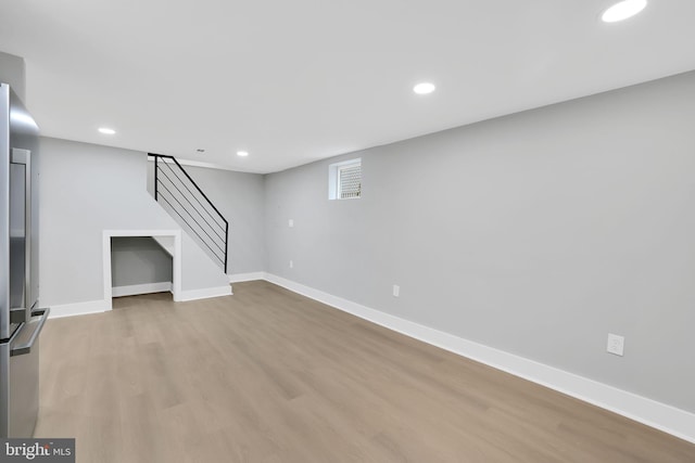 basement featuring light wood-type flooring and stainless steel refrigerator