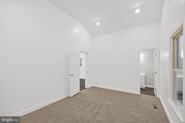 unfurnished bedroom featuring ensuite bathroom, dark colored carpet, and high vaulted ceiling