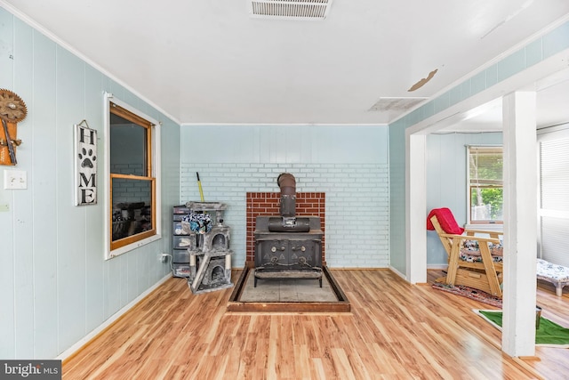 interior space with brick wall, wood walls, a wood stove, crown molding, and hardwood / wood-style flooring