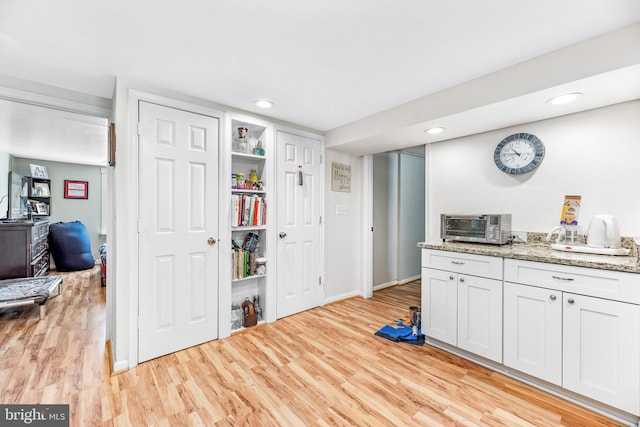 kitchen with white cabinets, light stone counters, and light wood-type flooring