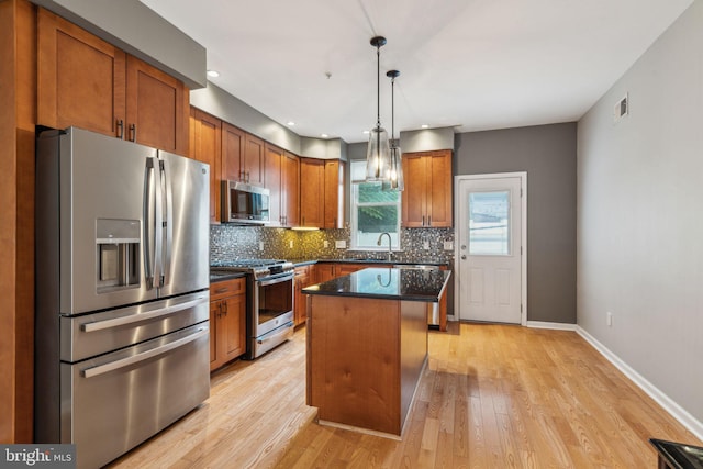 kitchen featuring light wood-type flooring, a kitchen island, backsplash, appliances with stainless steel finishes, and decorative light fixtures