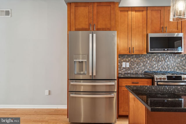 kitchen with light hardwood / wood-style flooring, dark stone countertops, appliances with stainless steel finishes, and tasteful backsplash