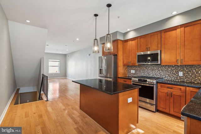 kitchen featuring pendant lighting, light hardwood / wood-style flooring, stainless steel appliances, a center island, and dark stone countertops