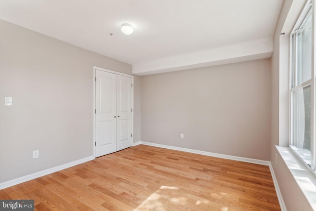 unfurnished bedroom with light hardwood / wood-style flooring, a closet, and multiple windows