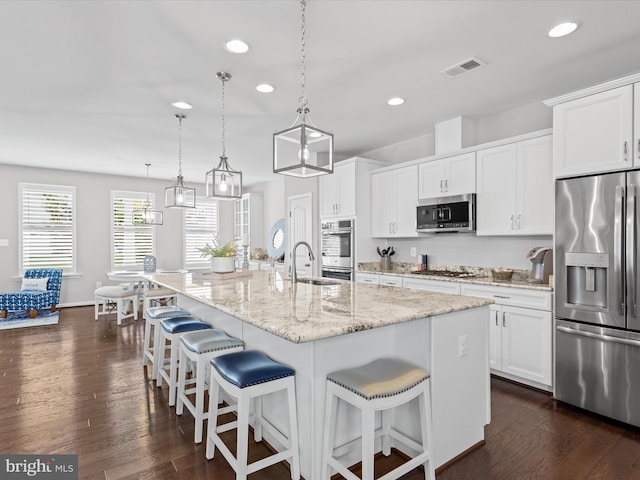 kitchen with appliances with stainless steel finishes, a center island with sink, dark hardwood / wood-style flooring, and pendant lighting