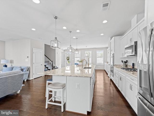 kitchen featuring white cabinets, an island with sink, stainless steel appliances, and dark wood-type flooring