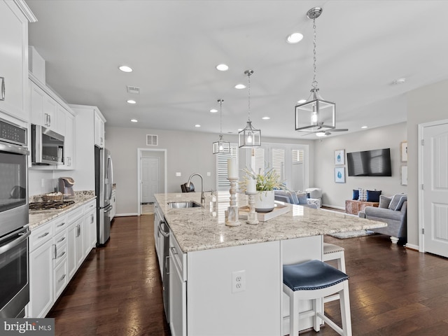 kitchen with ceiling fan, a center island with sink, white cabinetry, stainless steel appliances, and dark hardwood / wood-style flooring