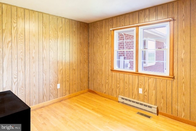 empty room featuring wooden walls, hardwood / wood-style floors, and a baseboard heating unit