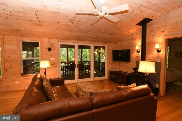 living room with ceiling fan, wood ceiling, a wood stove, vaulted ceiling, and light hardwood / wood-style floors