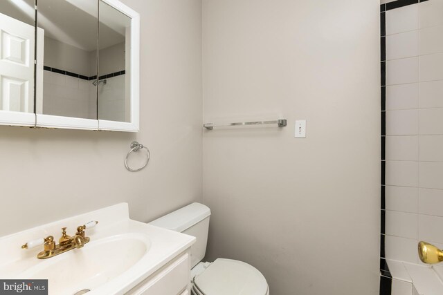 bathroom featuring a tile shower, vanity, and toilet