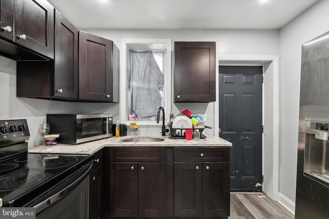 kitchen with light wood-type flooring, sink, dark brown cabinetry, light stone countertops, and black / electric stove