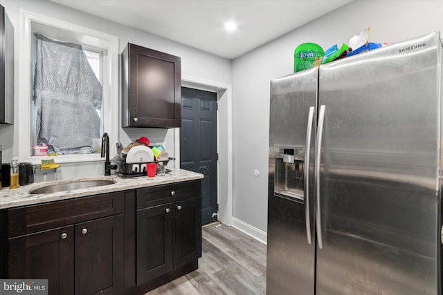 kitchen featuring light hardwood / wood-style floors, light stone countertops, dark brown cabinets, sink, and stainless steel fridge with ice dispenser