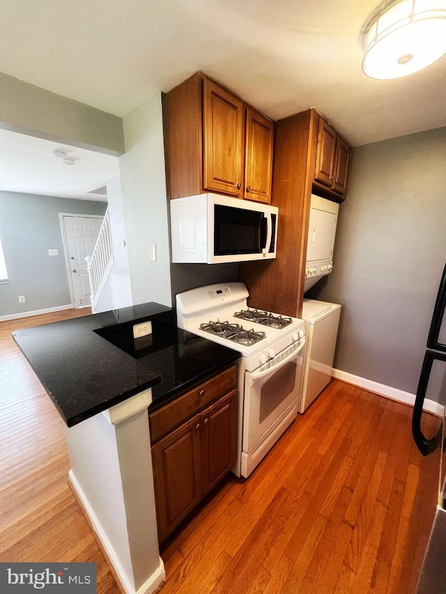 kitchen featuring white appliances, light wood-type flooring, kitchen peninsula, and stacked washer and clothes dryer