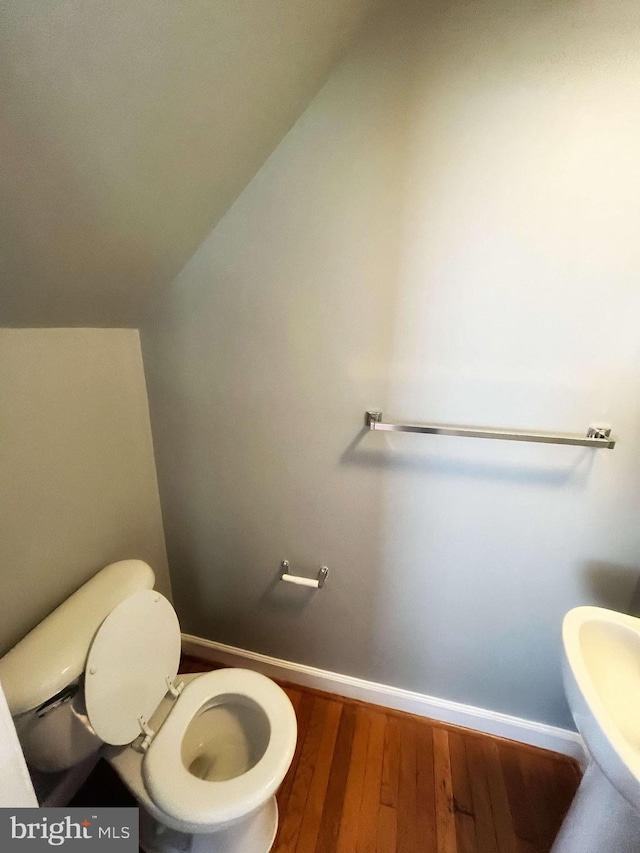 bathroom with toilet, hardwood / wood-style flooring, vaulted ceiling, and sink