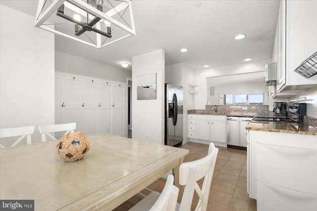 kitchen featuring light tile patterned floors, a chandelier, white cabinetry, stainless steel appliances, and dark stone countertops