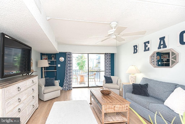 living room featuring light hardwood / wood-style floors, ceiling fan, and a textured ceiling