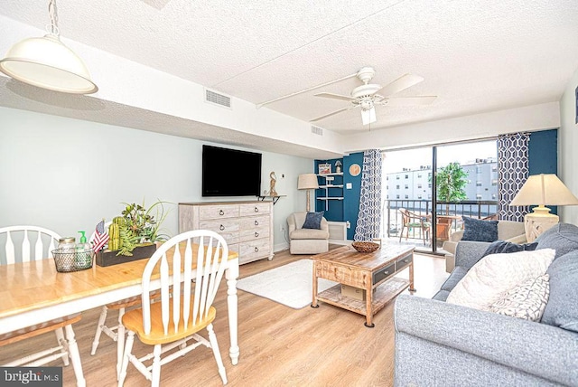living room with visible vents, light wood-style floors, ceiling fan, and a textured ceiling