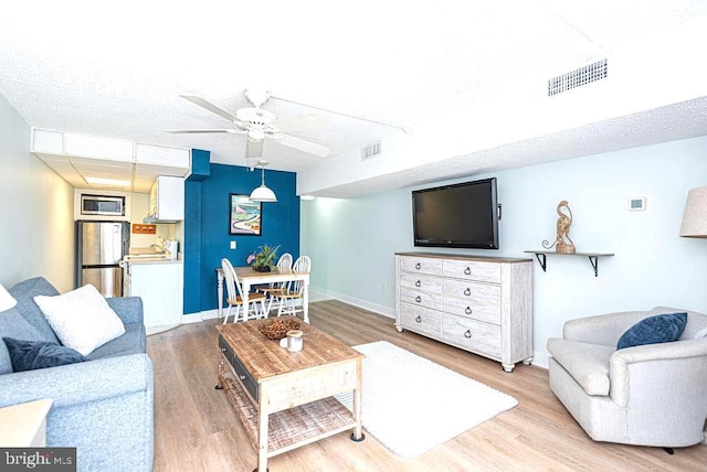 living room featuring light wood-type flooring, a ceiling fan, baseboards, and visible vents
