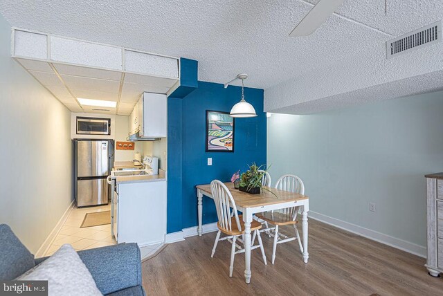 dining space with baseboards, visible vents, light wood-type flooring, and a paneled ceiling