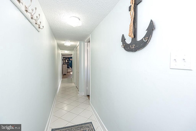 hallway with a textured ceiling and light tile patterned floors