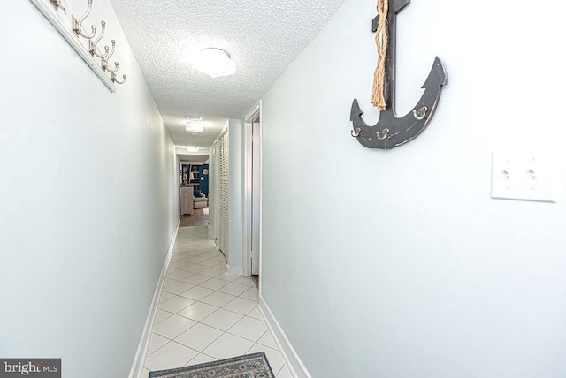 corridor with baseboards, a textured ceiling, and light tile patterned floors